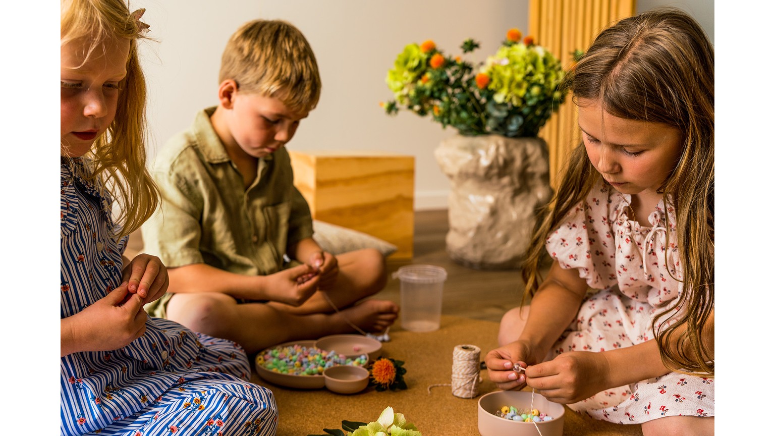 Børn sidder ved et bord og leger med små farverige perler og perleplader i varme toner